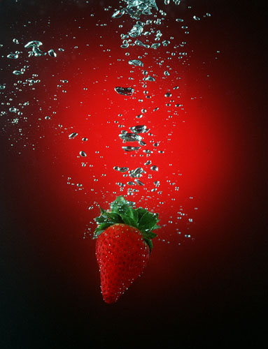 Strawberry in water with bubbles around it against a dark red spotlight